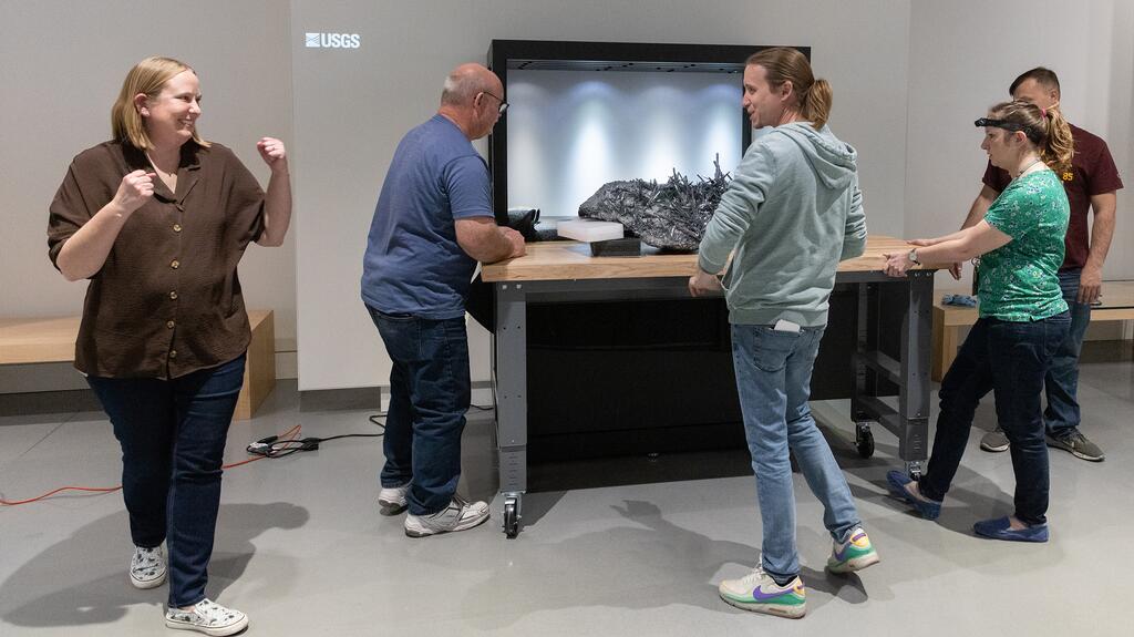 Violetta Wolf, director of the Alfie Norville Gem and Mineral Museum, (far left) celebrates as museum staff maneuver the stibnite specimen into its display case. (Credit: Chris Richards/The University of Arizona) Stibnite specimen Alfie Norville Gem and Mineral Museum